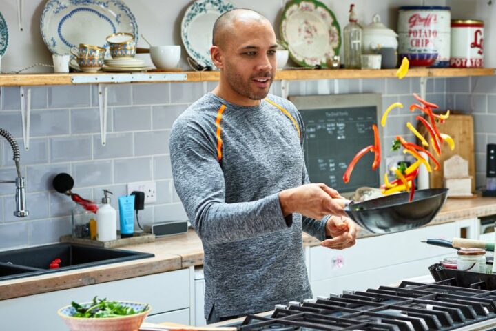 Man stir-frying vegetables in a wok in a home kitchen