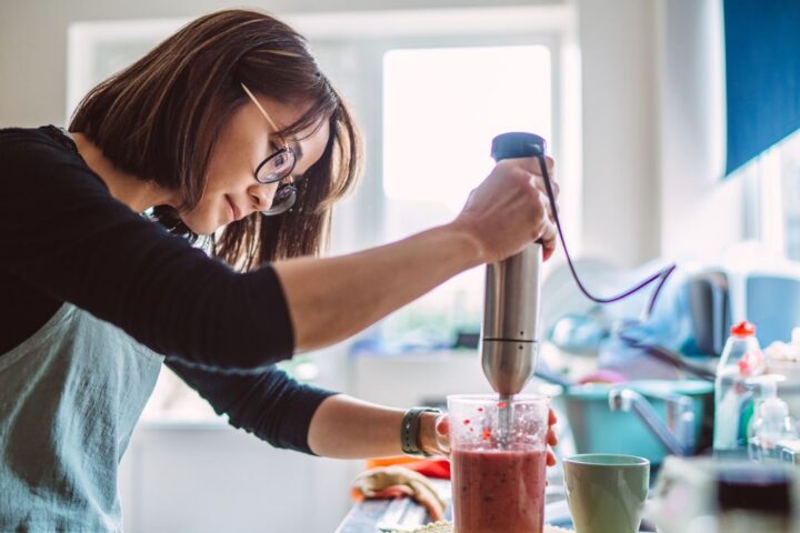 Woman making berry smoothie with stick blender