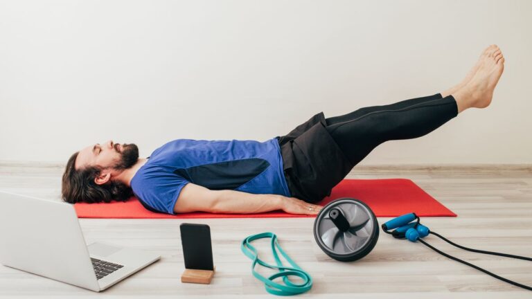 Man performs leg lowers with assorted exercise equipment on the floor around him