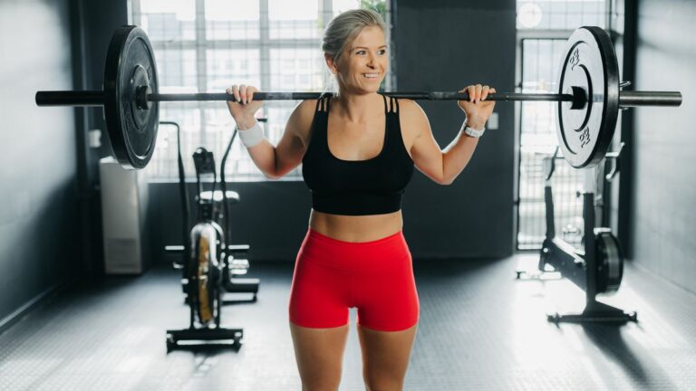 Woman holds barbell across her shoulders