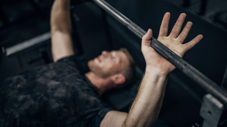 Man on a weight bench lying under a barbell in a gym
