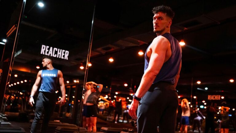 Barry’s Bootcamp trainer facing floor-to-ceiling mirror. The word Reacher is printed on the mirror