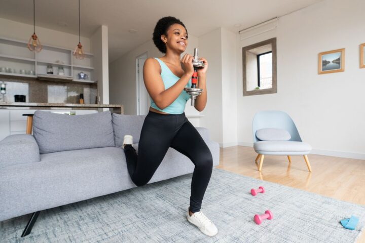 Woman performs Bulgarian split squat with her rear foot raised on a couch. She holds a dumbbell in front of her chest