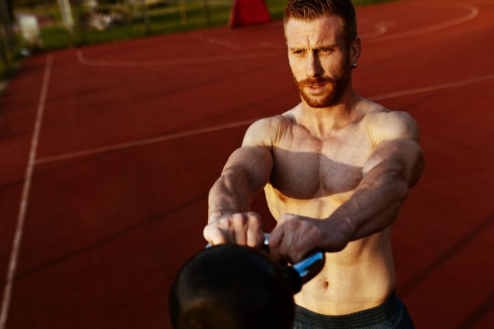 Shirtless man performing kettlebell swing